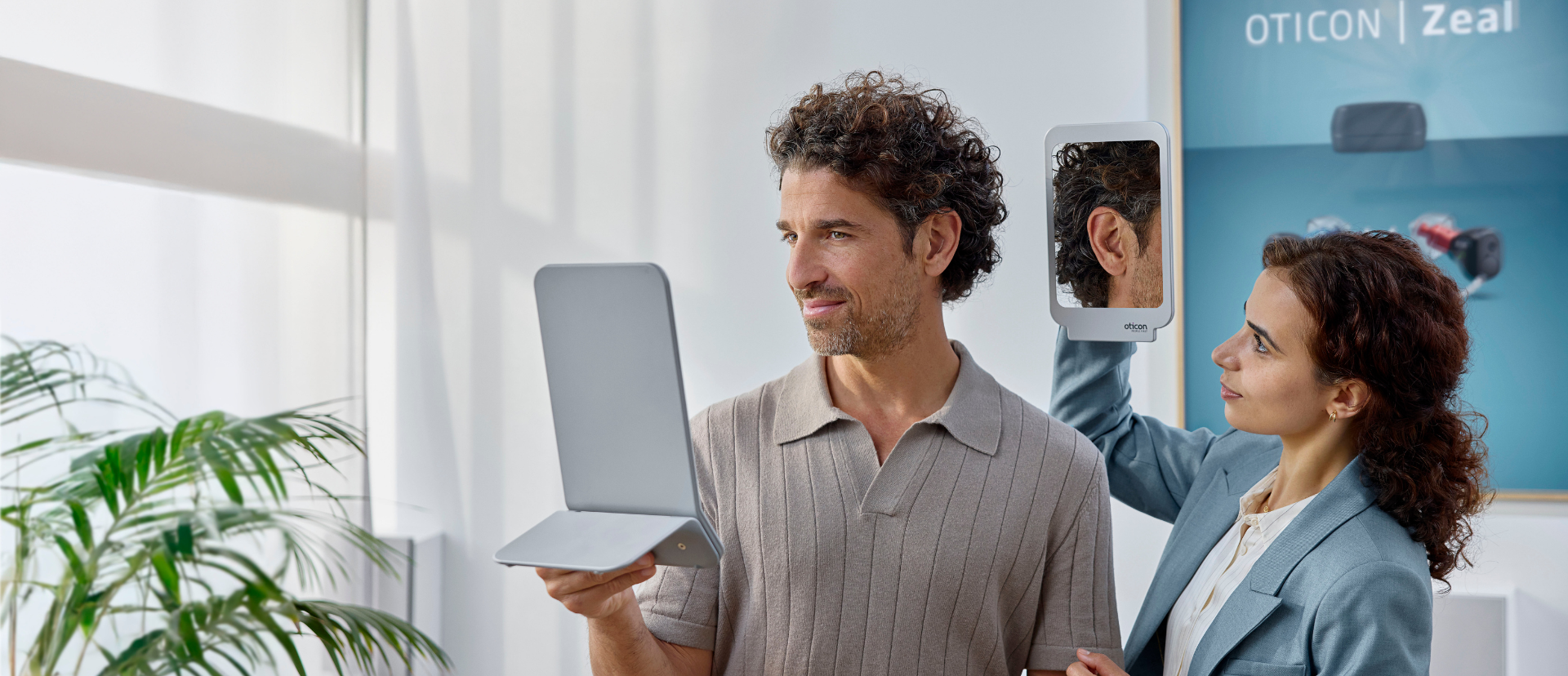 Male patient wearing invisible hearing aids and looking in the mirror, assisted by female Audiologist.