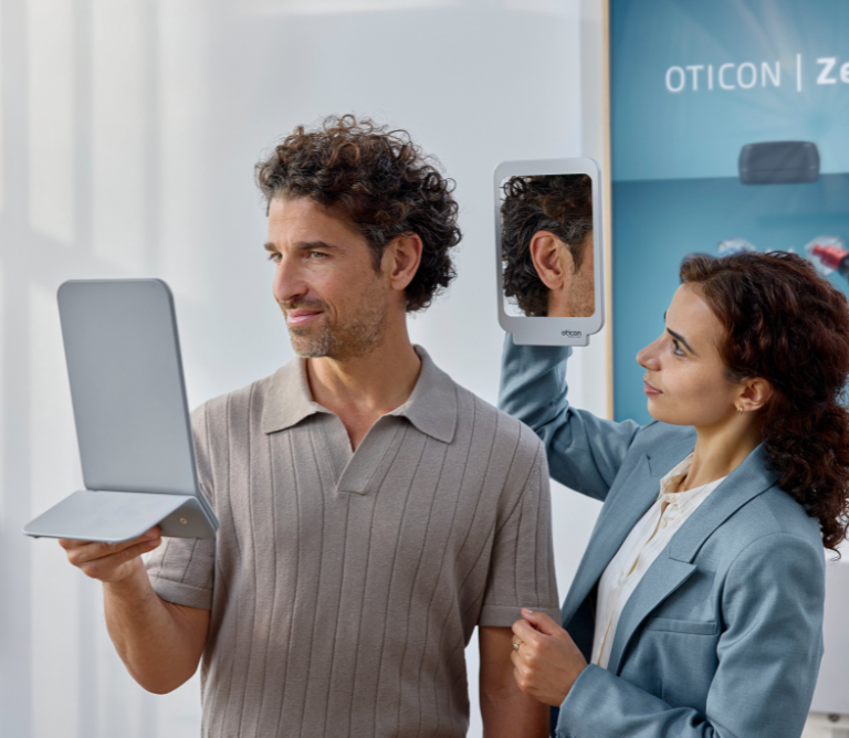 Male patient wearing invisible hearing aids and looking in the mirror, assisted by female Audiologist.