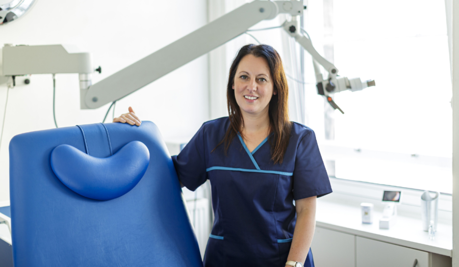 Melanie Jackson, Head of ENT Nursing and National Clinical Lead, stands in scrubs next to earwax removal treatment chair.